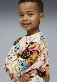 Camicia a maniche lunghe color crema con grafiche di gatti colorati in vari stili, con accenti neri, gialli e blu, tessuto morbido e vestibilità comoda.