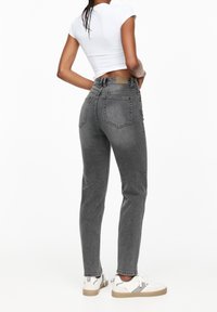 Jean gris taille haute avec une silhouette ajustée, design cinq poches, et fermeture à boutons, assorti à un haut blanc à manches courtes et des baskets.