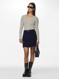 Ριγέ μακριά μανίκια, καΖακάκι με V-λαιμόκοψη σε κρέμα και μαύρο, συνδυασμένο με μίνι φούστα από μπεζ καμπαρντίνα. Μαύρες μπότες μέχρι το γόνατο και γυαλιά ηλίου.