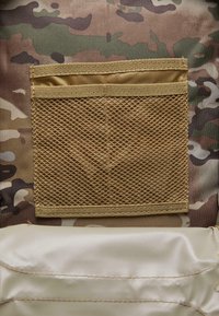 Tan mesh pocket on a camouflage background with a smooth, beige fabric section below, featuring light stitching.