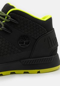 Czarno-neonowe żółte sneakersy Timberland z teksturowanej tkaniny, sznurowadłami, logo drzewa oraz wytrzymałą podeszwą w jaskrawożółtym kolorze.