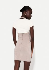 Strakke jurk met een witte top en gestreepte, nauwsluitende rok in gedempte kleuren. Voorzien van een hoge hals en korte mouwen met naaddetails.