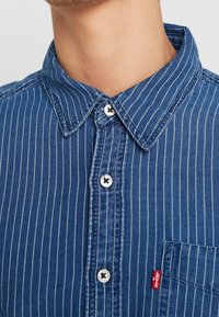 Blauwe gestreepte denim shirt met een button-down kraag, voorzien van witte knopen, een borstzak en een klein rood Levi's label aan de zijkant.