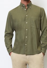 Košile na knoflíky v olivově zelené barvě, vybavená límcem, dlouhými rukávy, náprsní kapsou a bílými knoflíky podél předního zapínání.