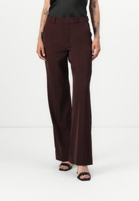Burgunderfarbene weite Hosen mit glatter Textur, Gürtelschlaufen und maßgeschneidertem Schnitt. Kombiniert mit schwarzen High Heels Sandalen.