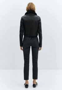 Czarna skórzana krótka kurtka z wysokim kołnierzem, zestawiona z ciemnymi dżinsami. Gładka tekstura, dopasowany krój i minimalne detale metalowe.