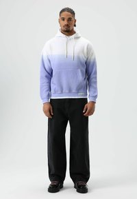 Pullover-Hoodie im Lavendel- und Weiß-Ombré-Design, mit Fronttasche, Kapuze mit Kordelzug und gerippten Bündchen. Kombiniert mit schwarzen, weit geschnittenen Hosen.