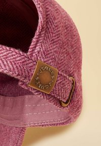 Șapcă de lână cu model în chevron roz, cu un emblema metalică bronz și o curea ajustabilă. Interiorul prezintă o captușeală fină.