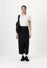 Svart denimskjørt med frontsplitt og sidelommer, kombinert med en hvit t-skjorte med korte ermer og svarte joggesko.