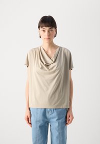 Béžový top s krátkými rukávy a volným střihem, vyrobený z měkké látky. Má lodičkový výstřih a minimalistické designové detaily.
