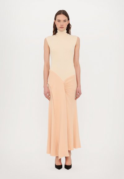 Robe sans manches, à col montant, avec un corsage ajusté en ivoire. Jupe fluide en pêche présentant un détail torsadé sur le côté. Texture lisse, longueur cheville.