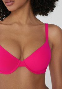 Růžový vycpaný podprsenka s hladkým povrchem, trojúhelníkovými košíčky a nastavitelnými ramínky. Bezešvý design, vhodný pro různé oblečení.