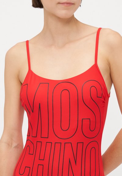 Rdeč kopalni kostum z tankimi naramnicami, ki ima velike črne črke, ki izgovarjajo "MOSCHINO." Gladka tekstura in prilegajoča zasnova.