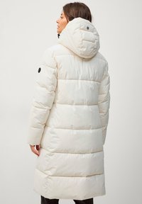 Manteau d'hiver long et gonflé de couleur crème avec une capuche. Présente des sections matelassées horizontales, des détails d'accent noir et une coupe ajustée.