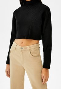 Svart kortärmad ribbad tröja med hög hals. Matchad med beige byxor som har framfickor och knappstängning.