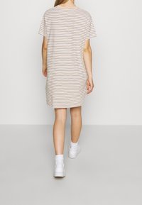 Beżowa sukienka krótki rękaw w pasiaki z cienkimi niebieskimi liniami. Luźny krój, długość do kolan, wykonana z miękkiego materiału. Noszona z białymi trampkami.