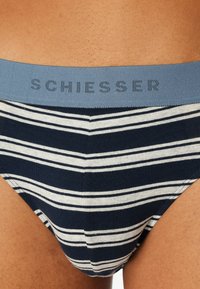 Slip da uomo a righe blu marino e bianche con una cintura elastica blu che presenta il nome del marchio "SCHIESSER" con una finitura testurizzata.