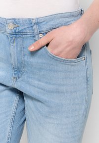 Lichtblauwe spijkerbroek met een aansluitend ontwerp, voorzien van een voorzak, zichtbare stiksels en een metalen knoop bij de taille.