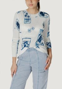 Maglione bianco con stampa blu caratterizzato da motivi tropicali e disegni floreali. Tessuto a maglia, maniche lunghe e polsini a coste. Abbinato a pantaloni azzurri chiari.