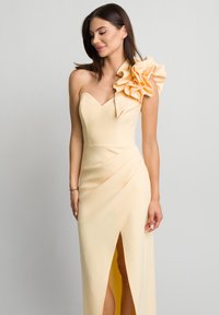 Sukienka bez ramiączek w kolorze żółtym z dużym falbaniastym akcentem na jednym ramieniu, z dopasowanym gorsetem i rozcięciem po stronie ud. Gładka faktura.