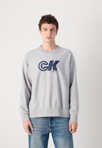 Šedá mikina s dlouhými rukávy, kulatým výstřihem a námořnickým logem s nápisem 'Calvin Klein' na přední straně. Volný střih a směs bavlny.