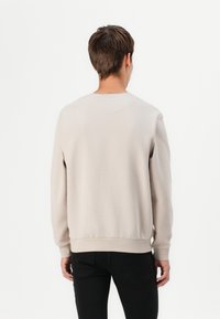 Světle béžová mikina vyrobená z měkké tkaniny, s kulatým výstřihem a žebrovanými manžetami. Jednoduchý design bez viditelných log či vzorů.