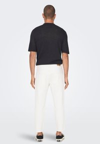 Camisa negra de manga corta, material ligero, combinada con pantalones blancos, ajuste entallado, con detalles en los bolsillos traseros y zapatillas negras.