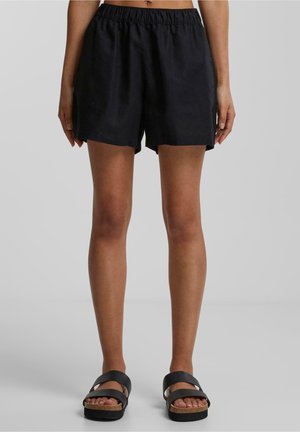 Schwarze Leinen-Shorts mit elastischem Bund, einem lockeren Schnitt und seitlichen Taschen, kombiniert mit schwarzen Sandalen mit Riemchen.