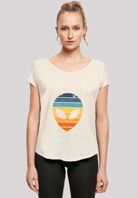 Cream-colored short-sleeve t-shirt with a distressed alien graphic featuring horizontal blue, orange, and yellow stripes.