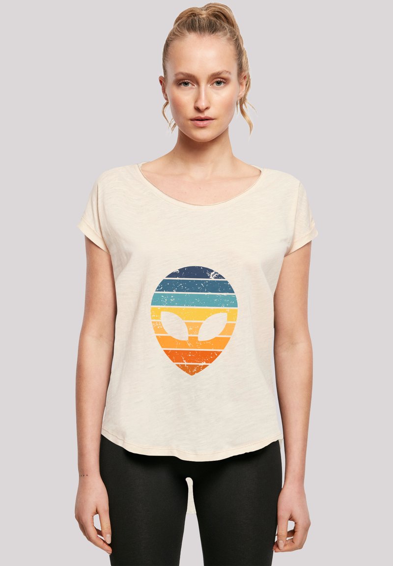 Cream-colored short-sleeve t-shirt with a distressed alien graphic featuring horizontal blue, orange, and yellow stripes.