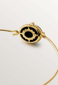 Collar de oro con una gema negra redonda enmarcada en un trabajo de metal ornamentado con patrones recortados, un diseño de alambre elegante y un acabado pulido.