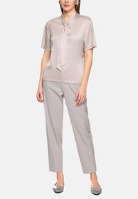 Light gray satin short-sleeve blouse with a tie neck detail, paired with light gray tapered trousers and metallic flats. Smooth texture.