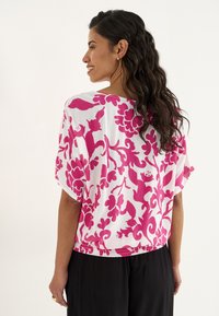 Korte mouw witte blouse met een gedurfde roze bloemenprint en een gathered zoom. Lichtgewicht stof met een lichte textuur en een relaxte pasvorm.