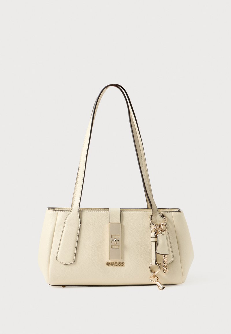 Geantă de mână de culoare crem, cu formă structurată, textură fină, două curele, accesorii aurii și un breloc decorativ.