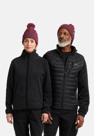 Giacca di pile nera con zip frontale e tasche laterali, abbinata a un berretto a maglia bordeaux con pom-pom. Gilet imbottito slim-fit in nero.
