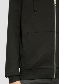 Schwarze Reißverschluss-Hoodie aus Baumwollmischung, mit vorderen Taschen sowie gerippten Bündchen und Saum. Glatte Textur mit minimalistischem Design.