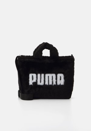 Sort faux fur taske med en fast form, der har et fremtrædende hvidt "PUMA" logo, korte hanke og en justerbar skulderrem.