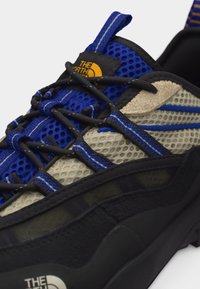 Modrá, béžová a černá síťovaná turistická obuv s černými tkaničkami, žlutým logem "The North Face" na jazyku a bílým logem na černé podrážce.