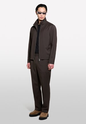 Brown zip-up jacket and matching pants made of smooth fabric, featuring a high collar and elastic waistband. Complemented by beige shoes.