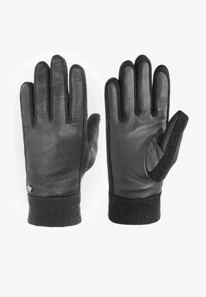 Schwarze Lederhandschuhe mit einer strukturierten Innenseite, gerippten Strickbündchen und einem Daumenloch. Mit einem metallischen Akzent im Handgelenkbereich.