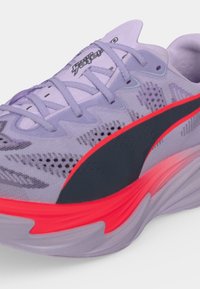 Chaussure de course violet clair avec une bande latérale noire et rouge, dessus en mesh respirant texturé et semelle épaisse amortissante.