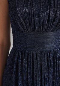 Tengerés plecate dress fényes, texturált anyagból. Ráncos derékkal és puha redőzéssel rendelkezik, ami folyékony sziluettet teremt.