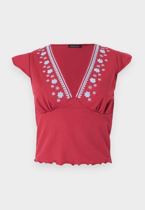 Rotes Kurzarm-Top mit tiefem V-Ausschnitt, blauer Blumenstickerei entlang des Halsausschnitts und Rüschensaum vor weißem Hintergrund.