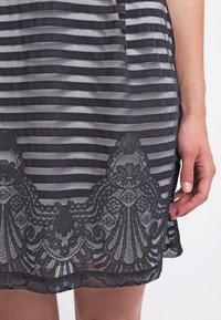 Gros plan d'une main à côté d'une jupe en dentelle à rayures horizontales noires et blanches avec des motifs floraux près de l'ourlet.