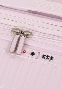 Gros plan d'une valise rigide rose clair avec double fermeture éclair, serrure TSA intégrée et combinaison numérique réglée sur 0-0-0.