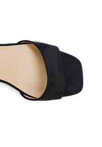 Zwarte suède slide-sandalen met een brede band en een vierkante teen. Gladde binnenkant, minimale textuur en geen zichtbare hardware.