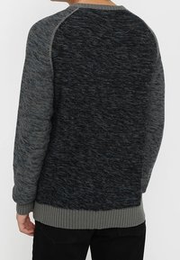 Gestrickter Pullover mit einer Kombination aus Grau- und Schwarztönen, gerippten Bündchen und Saum sowie einer strukturierten, weichen Stoffqualität.