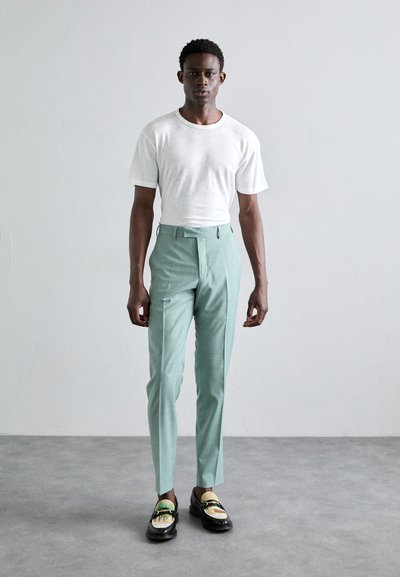 T-shirt branca de manga curta, calças ajustadas verde menta claras, sapatos mocassins pretos com detalhes dourados e verdes. Tecido suave, corte clássico, design minimalista.