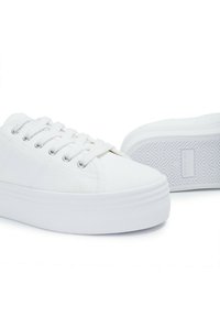 Baskets en toile blanches avec une semelle plateforme, dotées de œillets ronds en argent, de lacets plats et d'une semelle extérieure en caoutchouc texturé avec un motif en zigzag.