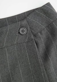 Szare spodnie na miarę z fakturowanego materiału z białymi prążkami. Posiadają czarny okrągły guzik w pasie oraz ostre, wyraźne linie.